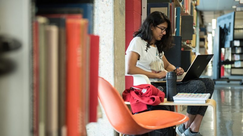 Female student studies in stacks with laptop