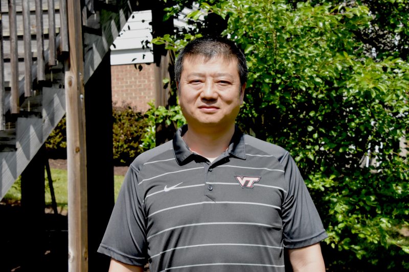 Shengfeng Cheng stands in his yard with trees in the background.