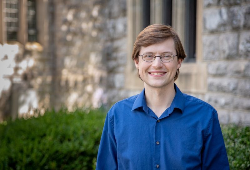 A man with reddish hair and a bright blue dress shirt poses for the camera.