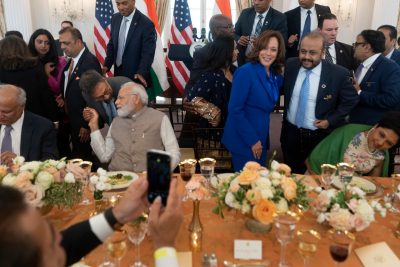 At a crowded banquet table atop a dais, people speak with one another,  including Indian Prime Minister Narendra Modi and U.S. Vice-President Kamala Harris.