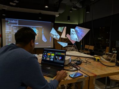 A man aligns projected digital imagery onto suspended geometric forms in the Expressions Lab at Amazon HQ2 during the workshop “Projection Mapping.” Photo by David Franusich for Virginia Tech.