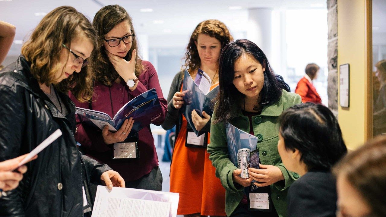 several female students standing around a display table speaking with a guest