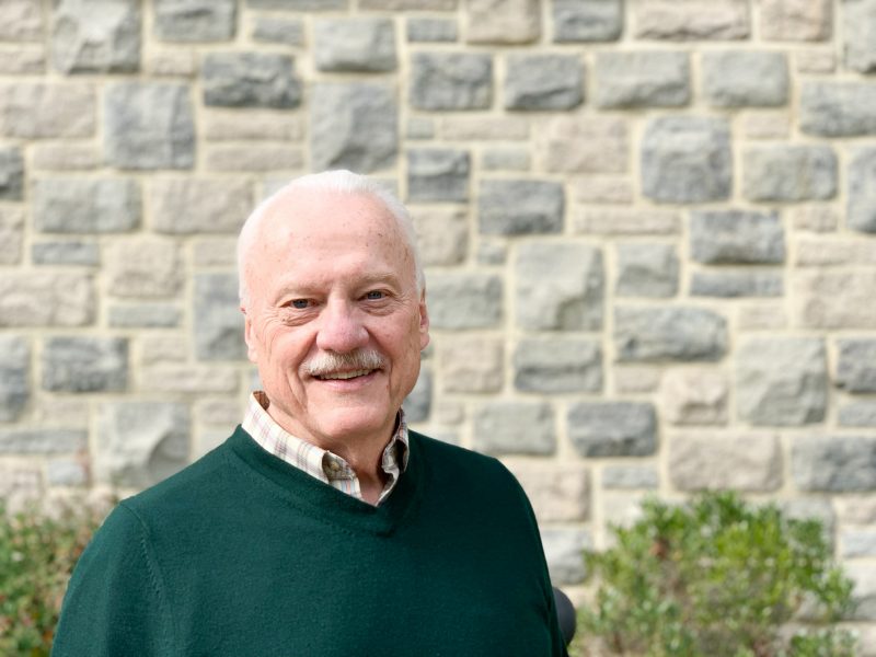 Tom in forest green sweater outside in front of Hokie stone wall