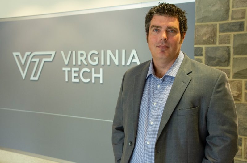 Pollyea in suit posed in front of VT logo inside North End Center