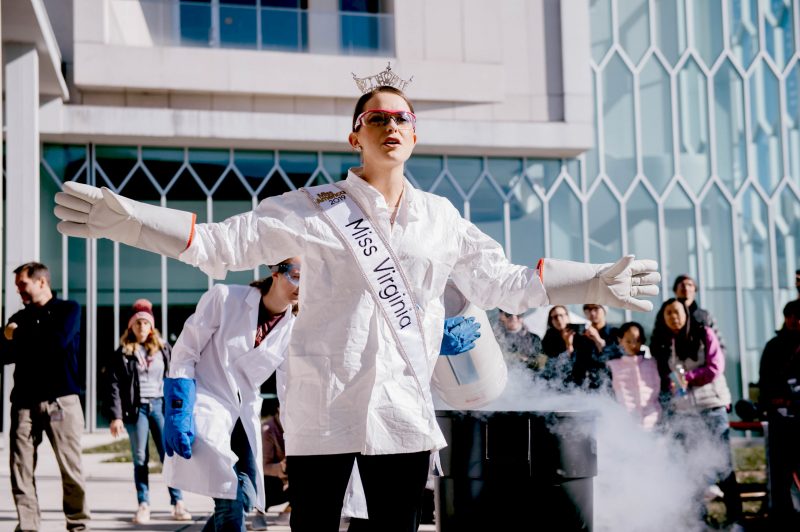 Camille performs chemistry demo outside Moss Arts Center with lab coat, Miss Virginia sash and crown and hot pink jeweled lab safety glasses