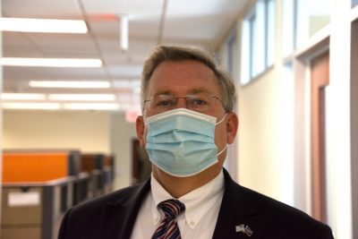 man stands wearing mask and cubicles recede in background