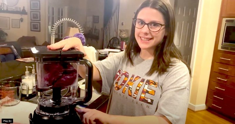 Woman stands in home kitchen with blender and smiles at camera