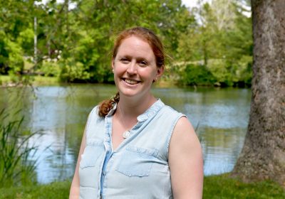 woman with red hair smiles in front of Duck Pond on a sunny day