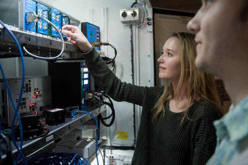 female is changes wires in a cabinet of circuitry and IT systems with male in foreground