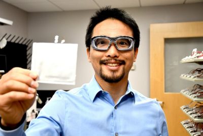 man in blue collared shirt wears safety glasses and holds up a pouch battery