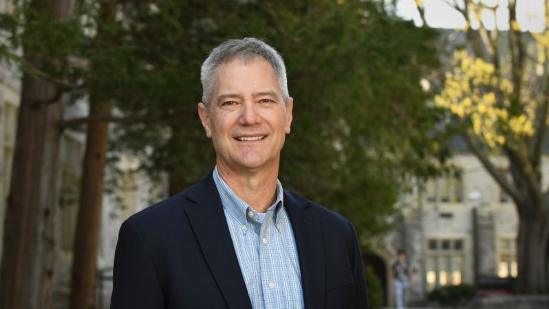 Kevin Pitts in navy blazer outside with trees and campus buildings