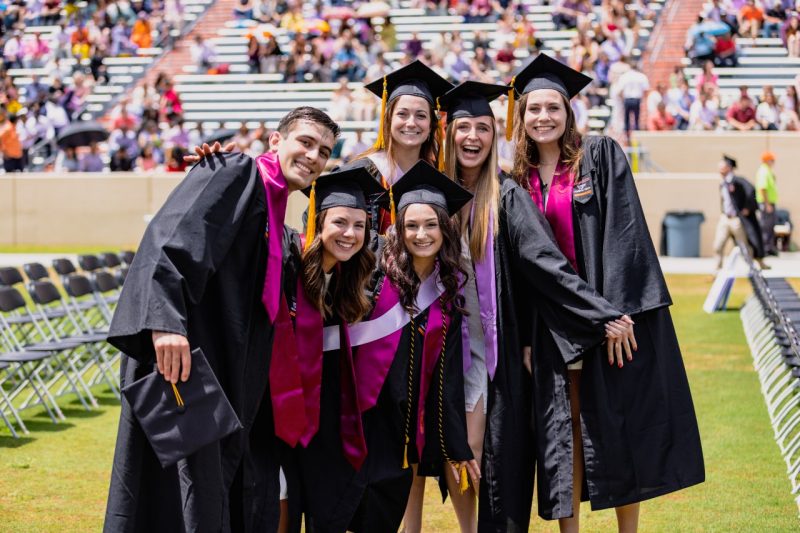 group of graduates huddle on football field in caps and gowns