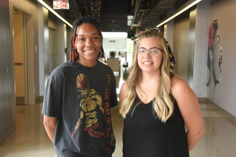 2 young women stand in a long hallway and look at camera