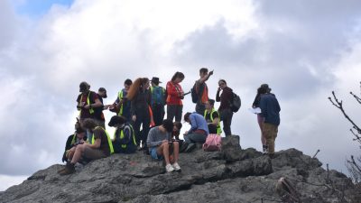 students sit and stand on top of mountain for class