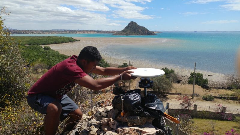 man squats and adjusts equipment on beach view of Madagascar