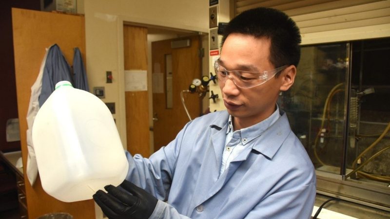man wearing safety clothing and googles holds a gallon water jug