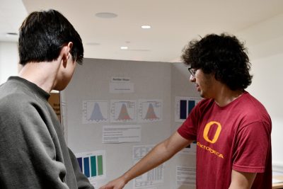 A student points to information on poster board, while another student looks on.