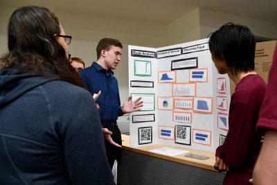 Student discusses his poster board while small group surrounds him.