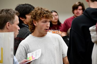 Student and judge in foreground with larger group of students in background.