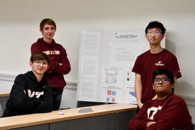 Group of four students standing next to poster.