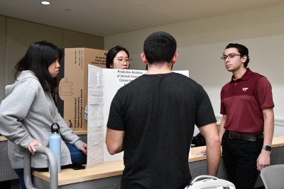 One individual with back to camera speaks to three students surrounding their poster.