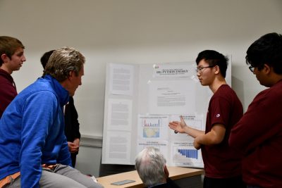 Group of individuals watch poster presentation by a student.