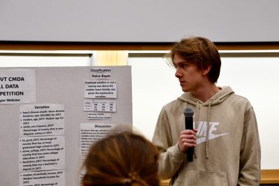 Student with microphone next to poster board.