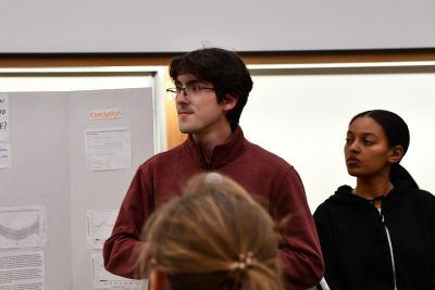 Two students next to poster board stand listening.