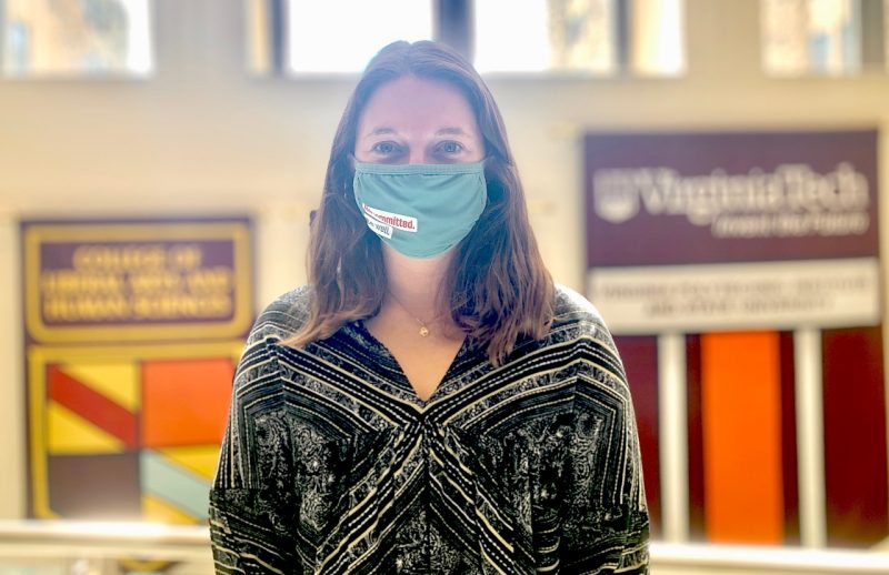 Jordan Fox, wearing a blouse and COVID-style face mask, poses for a photograph near some windows.