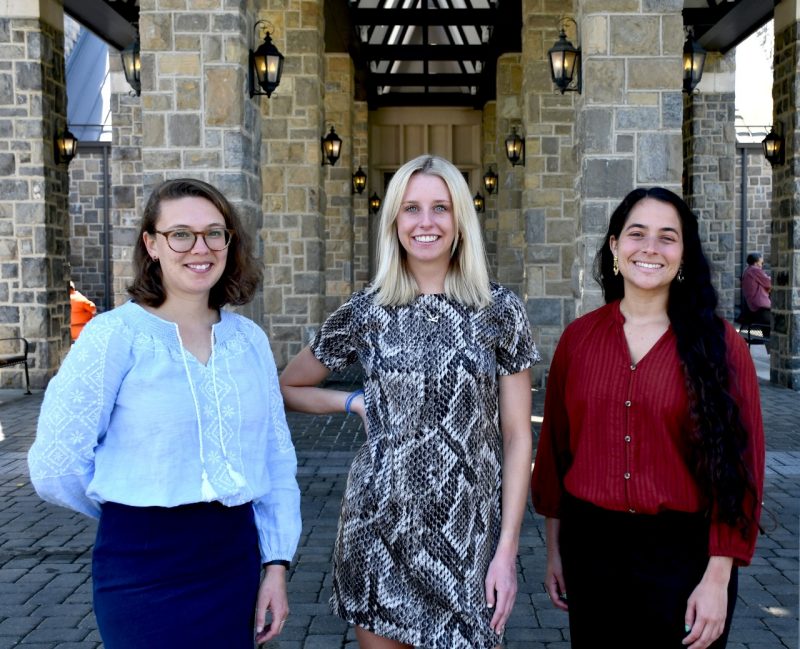 Three female students pose beside each other under the Hokie Stone columns at the entrance of the Inn at Virginia Tech.