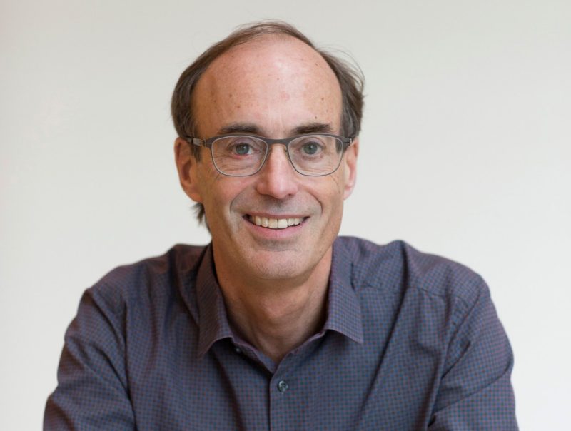 A man with glasses poses for the camera wearing a blue shirt.