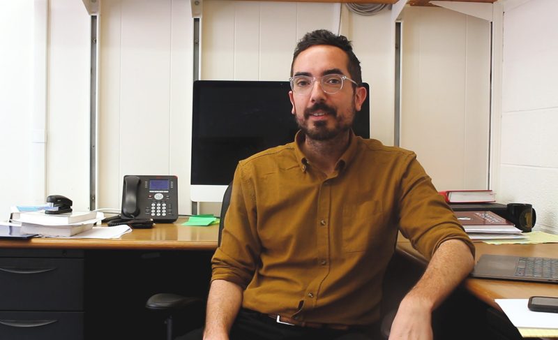 Shoemaker sitting at desk looking at camera