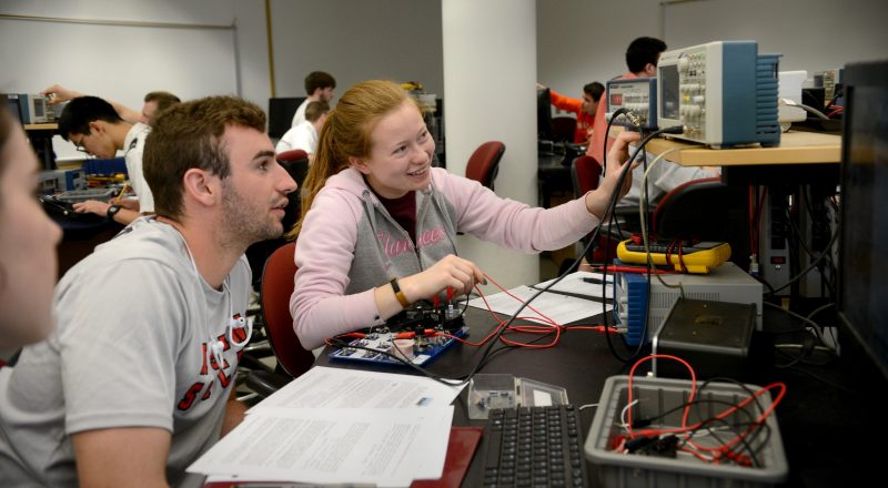 redhead female student at desk with brunette male classmate smiling and looking at data from experiment