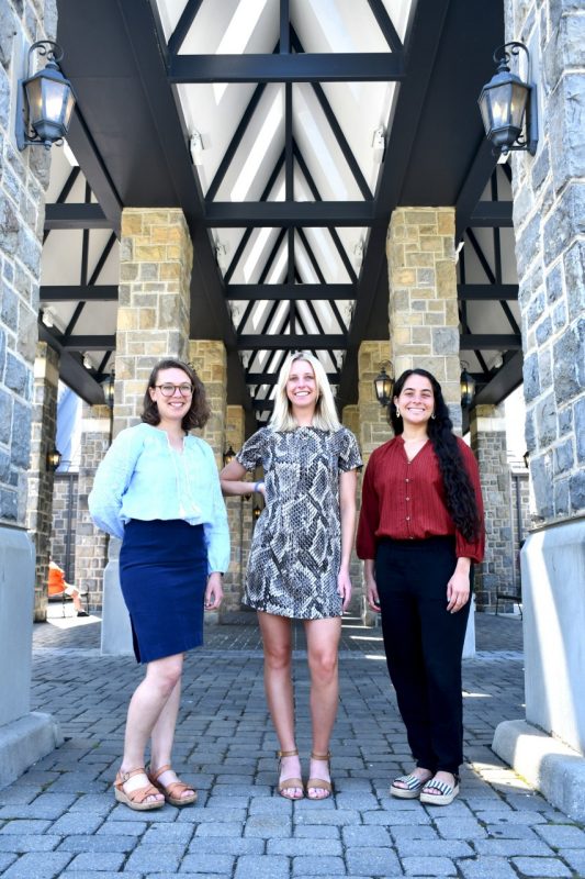 three women stand in between stone columns and smile