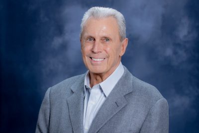 man with white hair and gray suit smiles for portrait