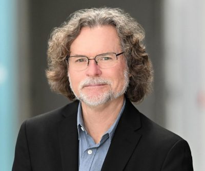 man with glasses, shoulder length curly hair, and graying beard portrait