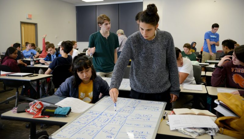 Students participate in a math class at the Surge Space Building, with one girl standing and using a marker on a dry erase board, in this 2018 photo. Photo by Natalee Waters for Virginia Tech. 