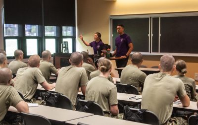 ew cadets sit in a classroom facing two Weeks of Welcome leaders as they instruct the class.
