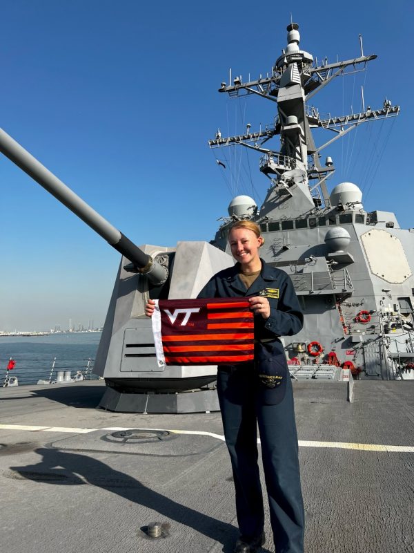 Loffert stands on board a U.S. Navy ship holding a Virginia Tech flag.