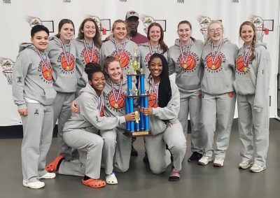 Eleven women cadets gather around the trophy in two rows with their coach. They have medals around their necks and are all smiling.