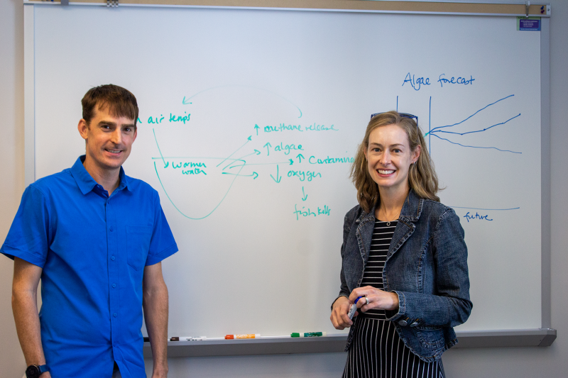 This image shows Quinn Thomas and Cayelan Carey in front of a whiteboard.