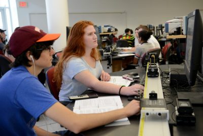 Male and female students look at computer and change dials during a physics lab.
