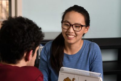 female therapist smiles at teenage client and works through a workbook.