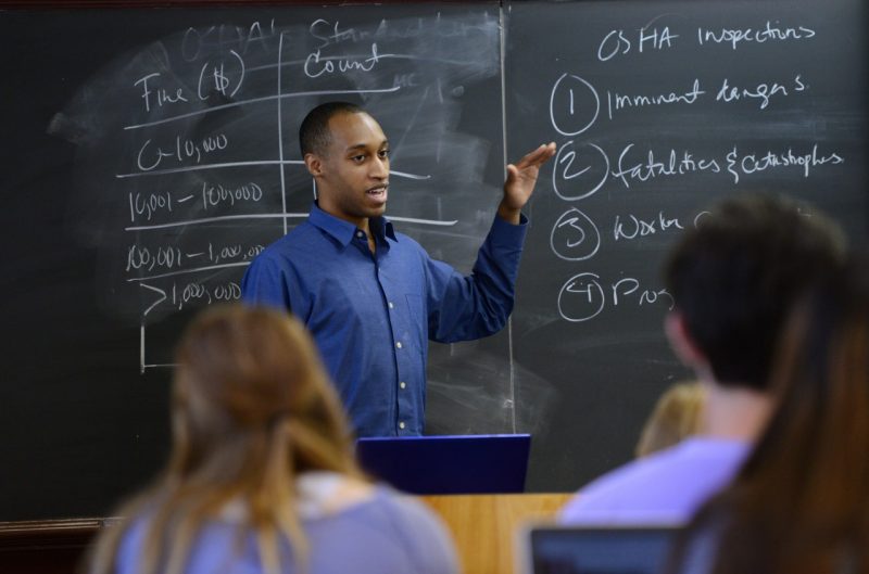 Male instructor references chalk board in classroom.