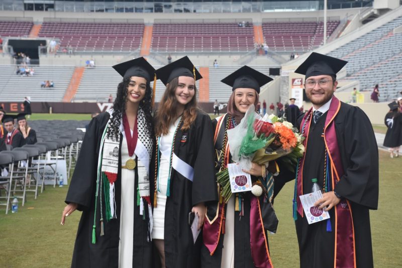 four graduates pose and smile in stadium