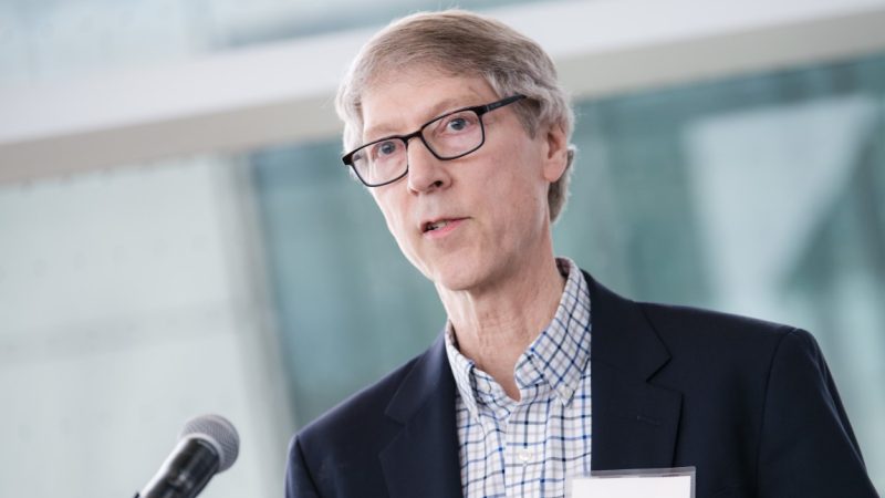 middle age man with glasses and business casual blazer speaks at microphone