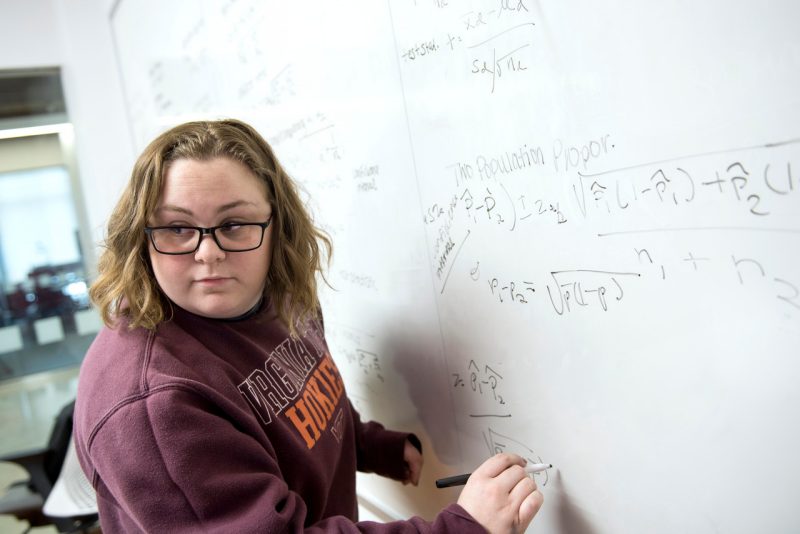 female student writes on white board and turns back to look at classmates