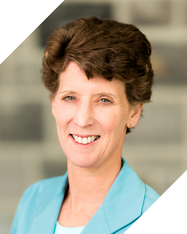 woman with turquoise blazer poses with blurred rock wall in background. photo is framed by angled corners