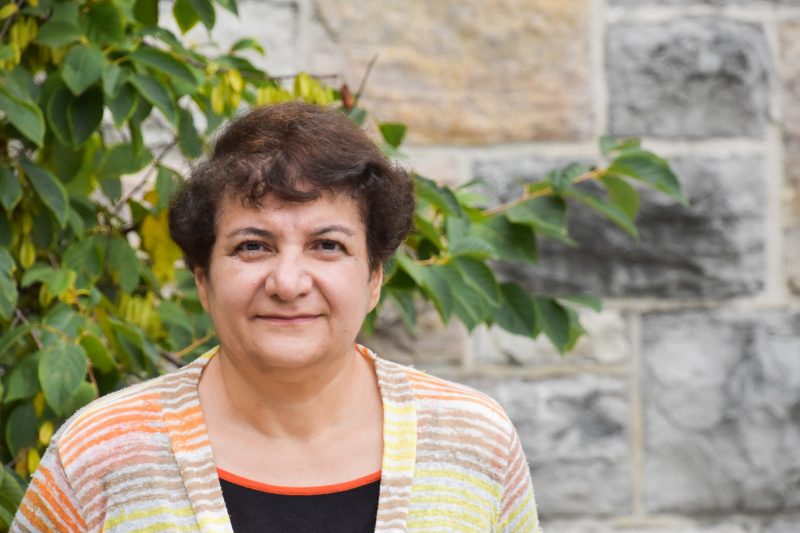 Giti stands outside in front of Hokie stone wall and tree with green leaves