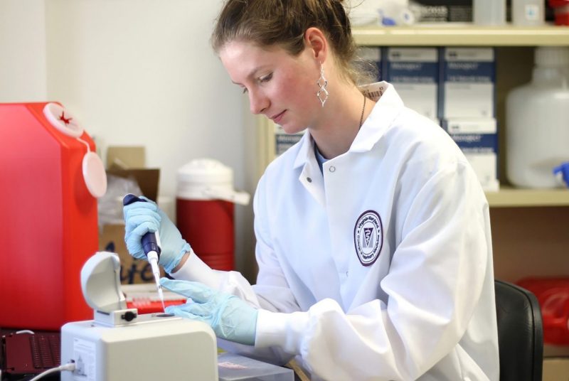 Amber in lab coat pipetting into centrifuge tubes in rack